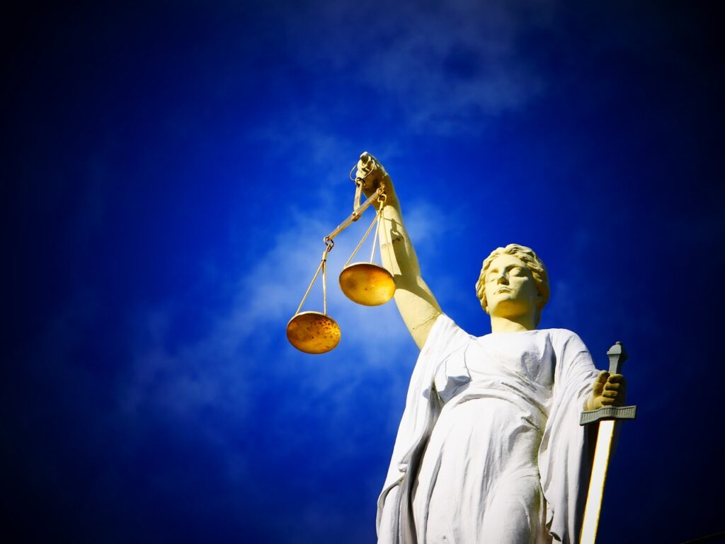 Statue of a woman holding scales and a sword, symbolizing justice, set against a clear blue sky background.