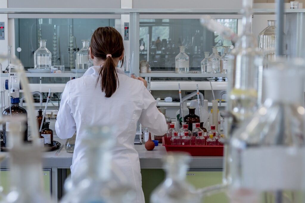 A woman wearing a lab coat stands in a laboratory, surrounded by various scientific equipment and glassware.