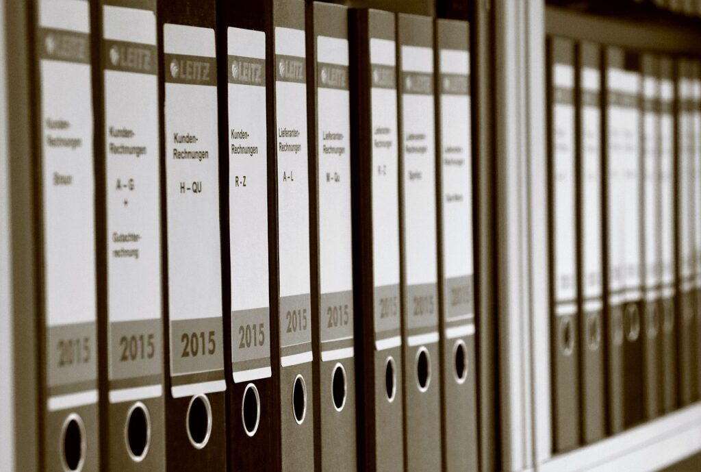 A row of labeled binders on a shelf, containing documents from 2015, organized alphabetically by client names and order of appearance.