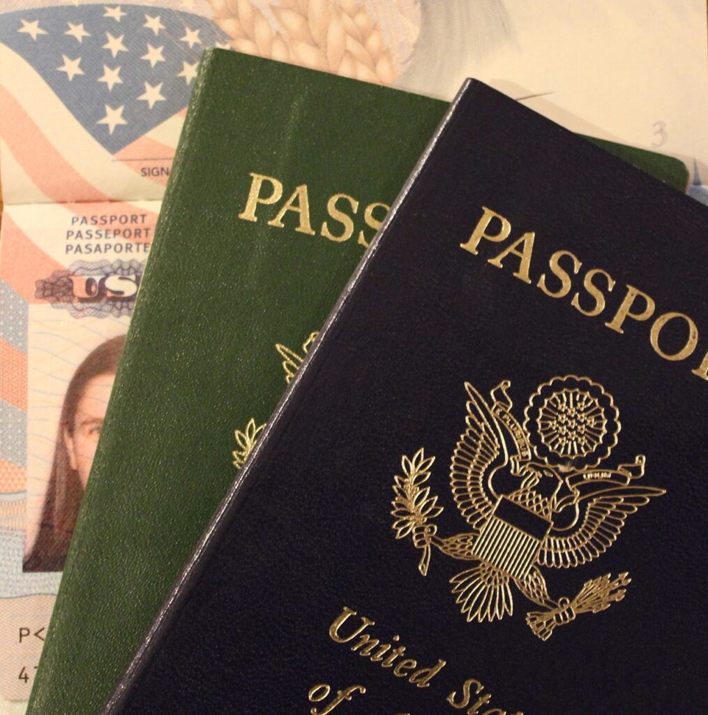 A close-up of two passports with a visible photograph page in the background, showing parts of an identification photo and the American flag.