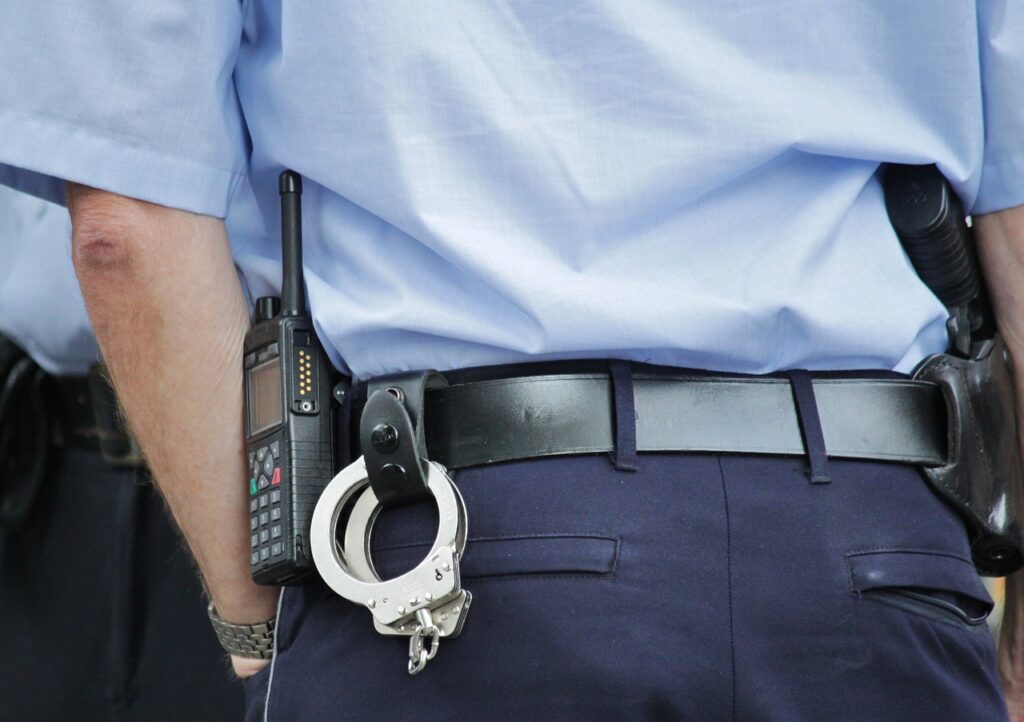 A person in a police uniform with a walkie-talkie, handcuffs, and a holstered weapon attached to their belt.